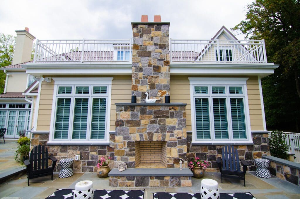 A natural stone fireplace on an outside patio sitting against a house.