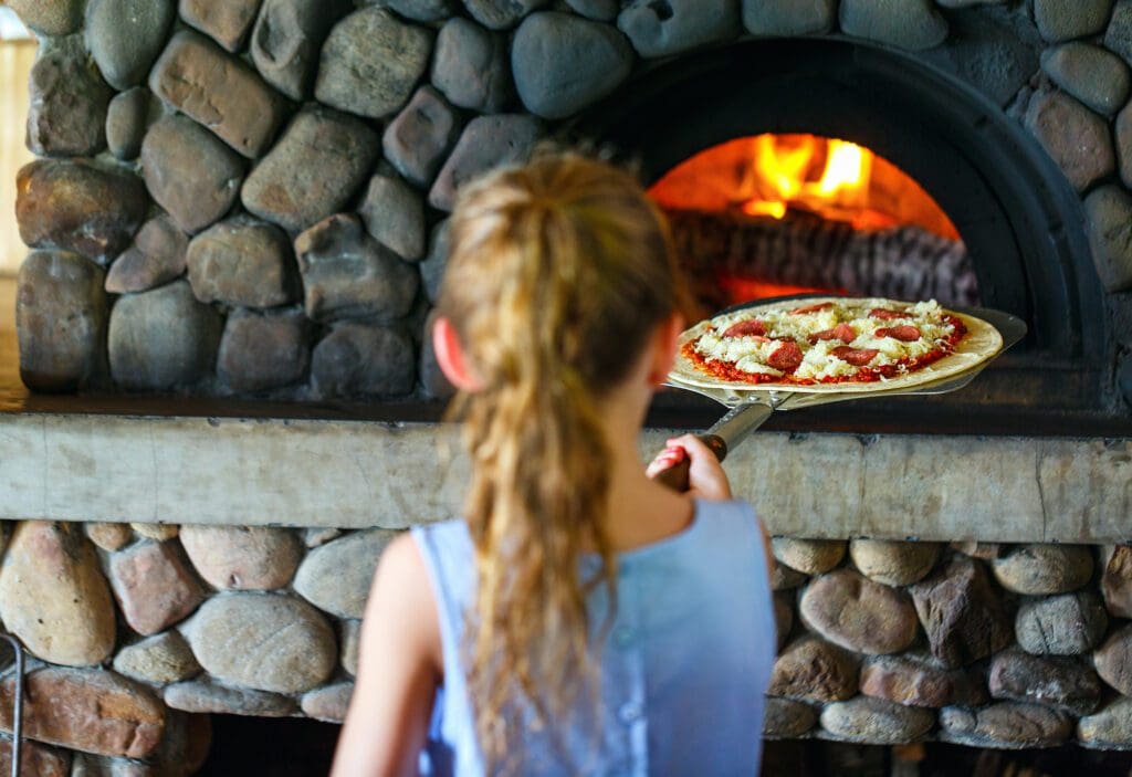 Young girl putting pizza into an outdoor pizza oven