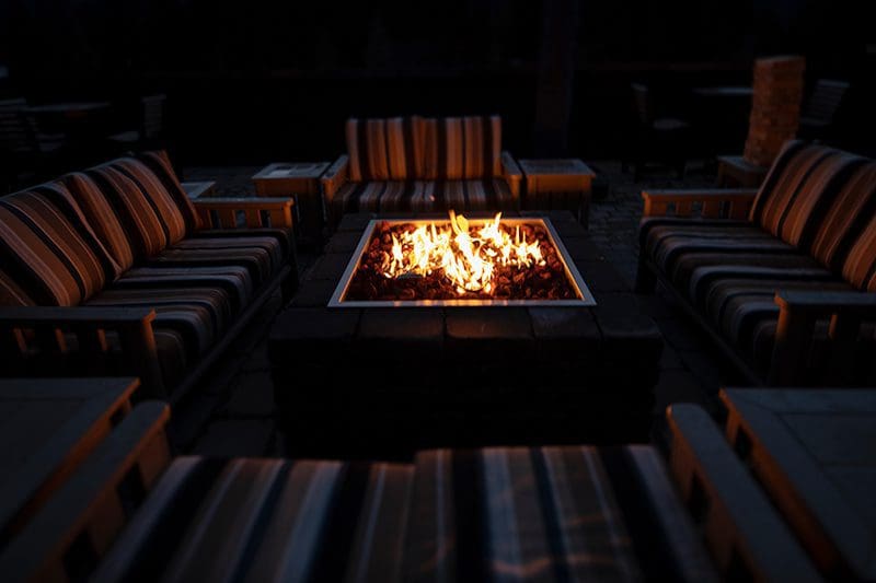 A gas-powered fire table burns with flames, surrounded by outdoor furniture.