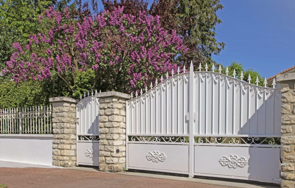 Stone piers hold up a gated driveway entrance with trees in the background.